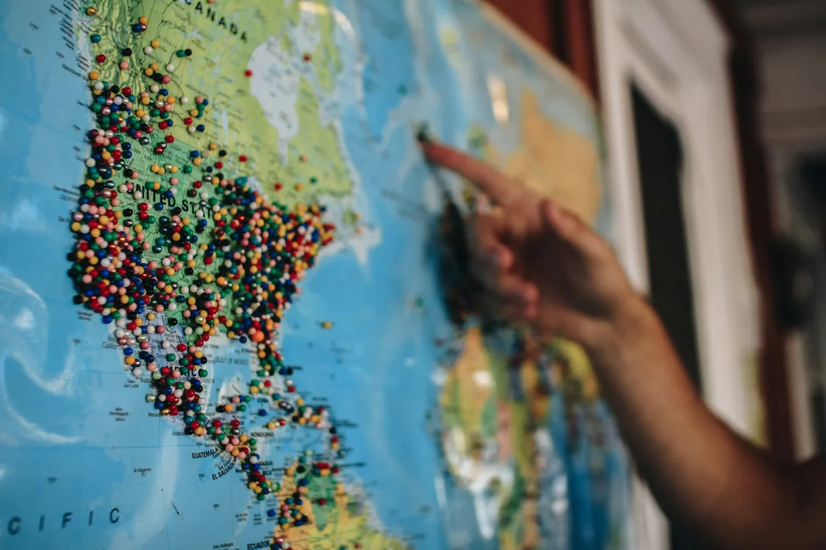A hand pointing at a map with pins in it