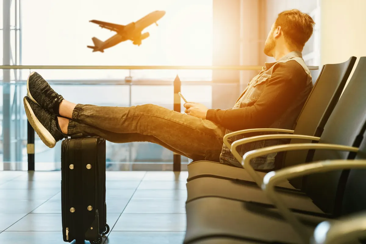 A traveller with his feet up on his suitcase, watching a plane take off